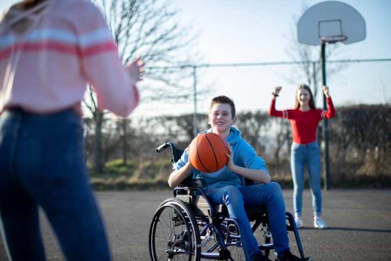 teen wheelchair user plays basketball with two teenage women outdoors